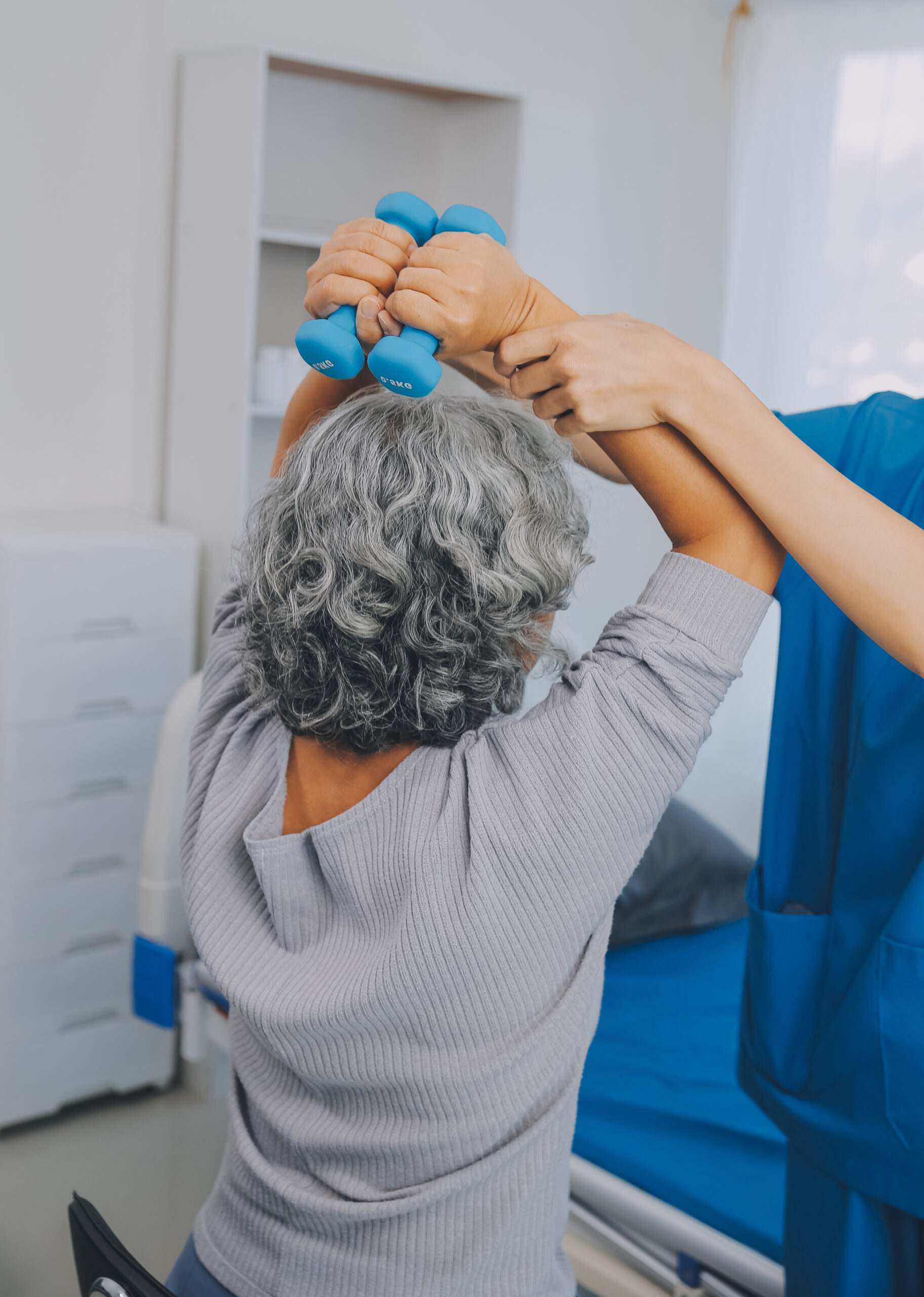Old woman training with physiotherapist using dumbbells at home.